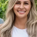 Blonde woman poses in front of foliage in a white shirt